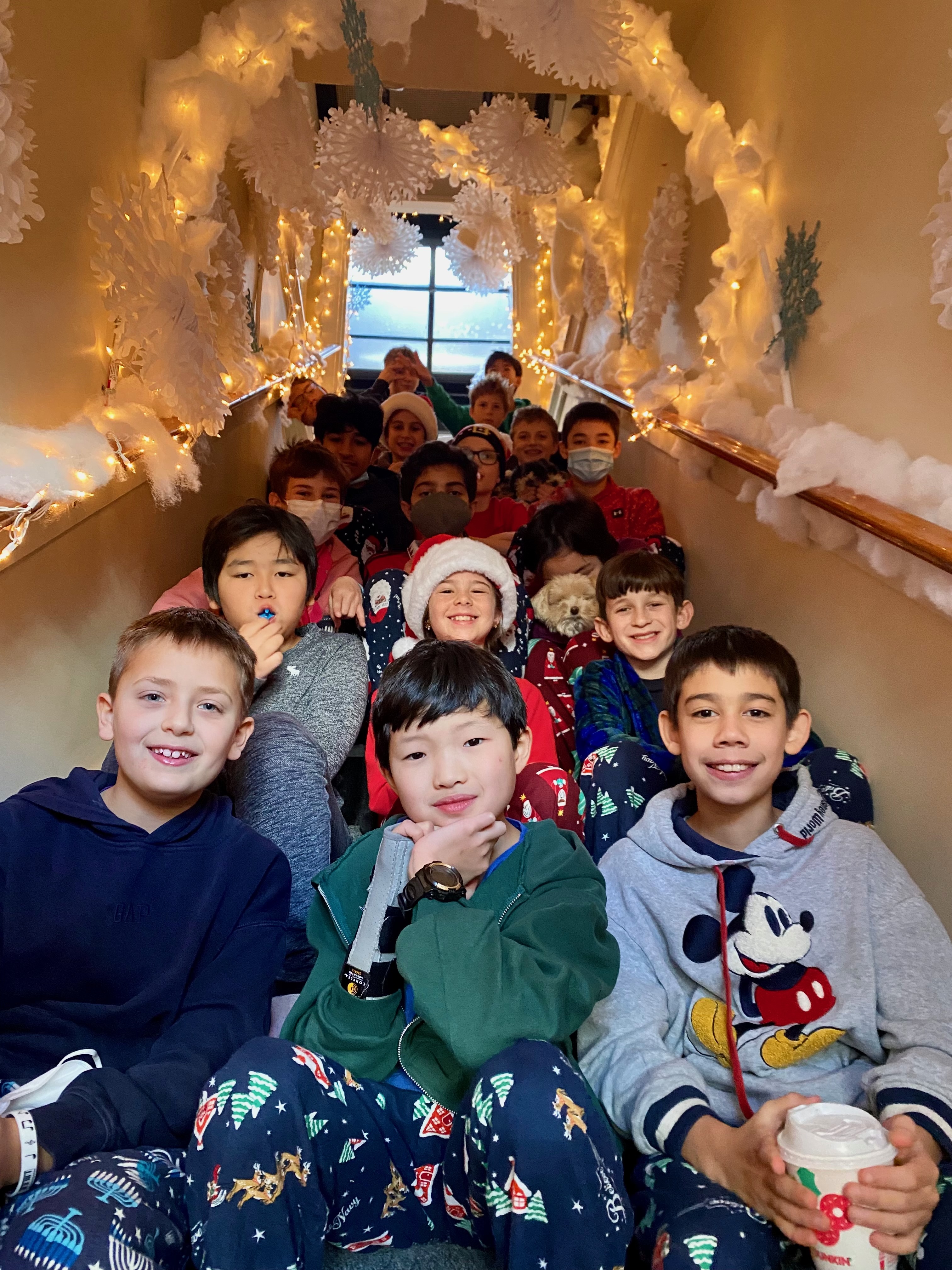 WSA students in festive pajamas gathered together on a string-light-decorated staircase
