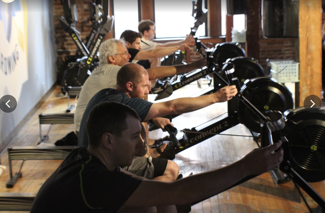 A row of people pulling on Concept2 rowing machines inside the brick-walled Power Rowing studio